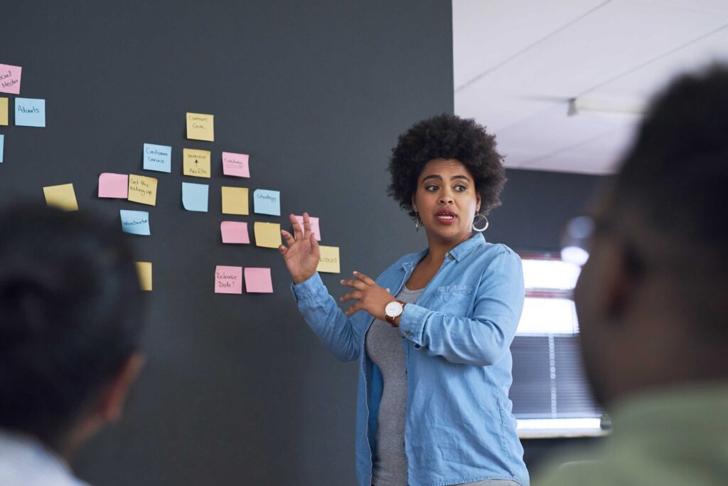 Woman speaking in front of a wall covered with post-it notes.